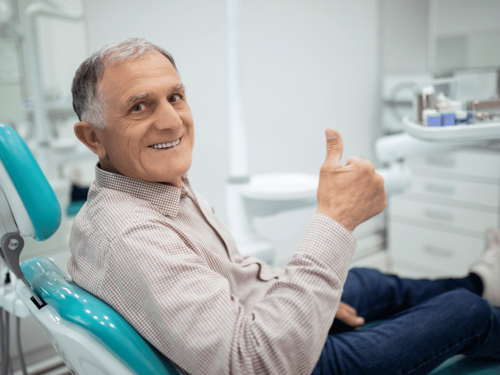 a man in a dental chair with his thumb up happy with his tooth implant vs dental bridge choice