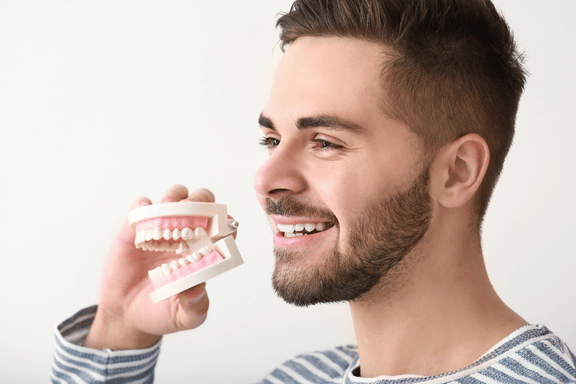 man showing off his new profile and holding dental model after an oral surgeon repaired his facial injury